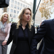 Elizabeth holmes walks hand in hand with Noel Holmes and Billy evans while people take pictures around her.